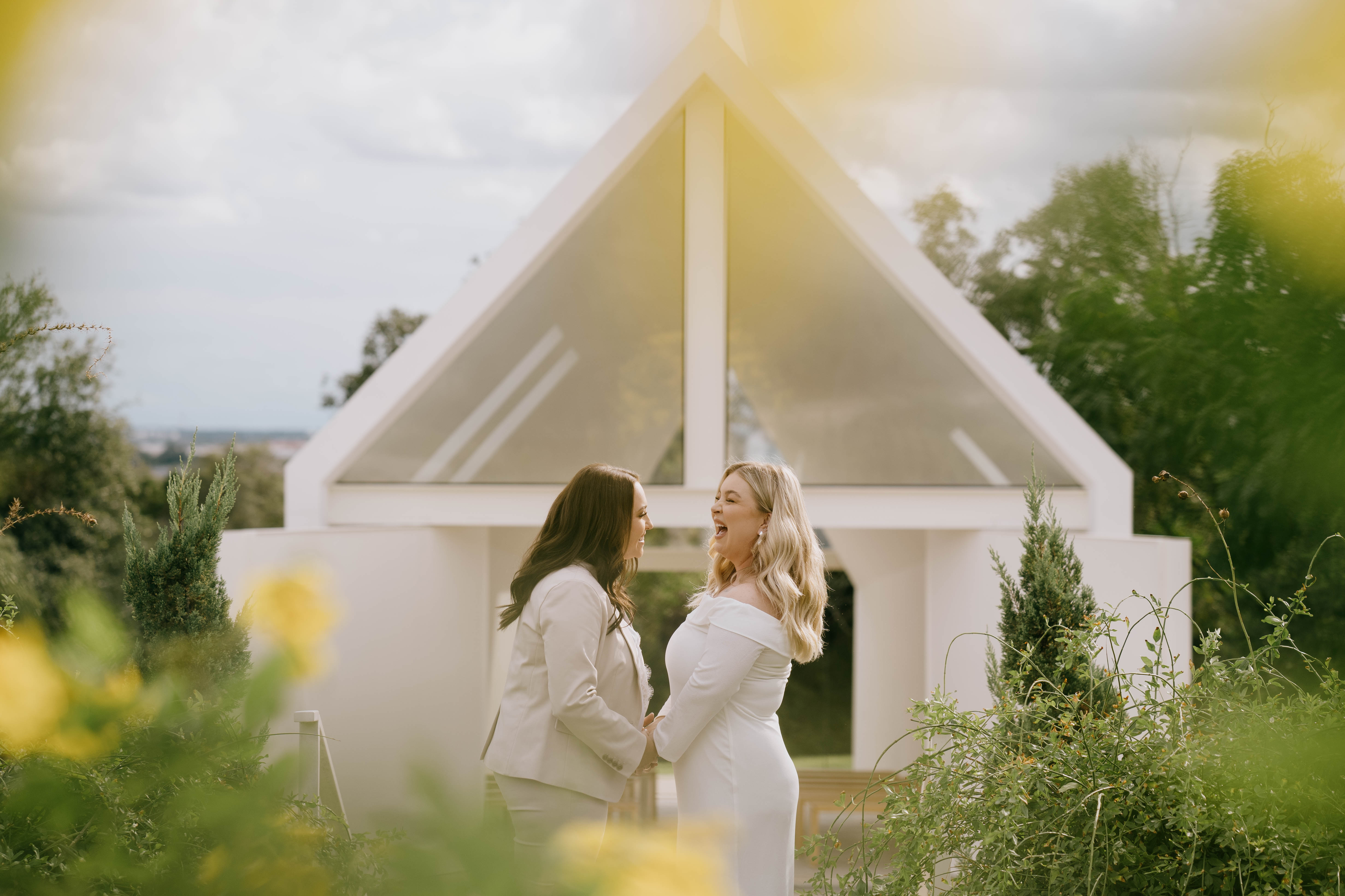 Brides laughing and framed in flowers outside of modern wedding venue in Georgetown, Texas